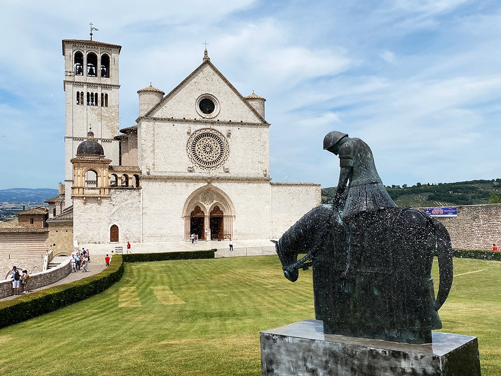 assisi cathedral with modern statue of horse and rider in foreground