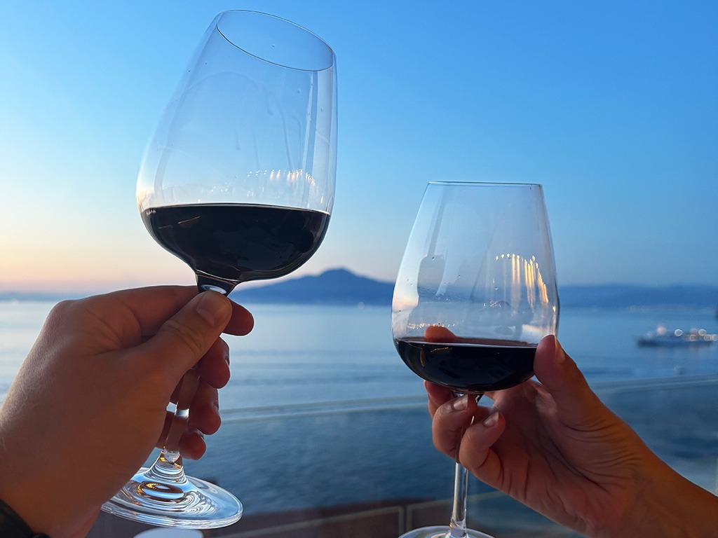 two red wine glasses with the bay of naples and mount vesuvius in the background