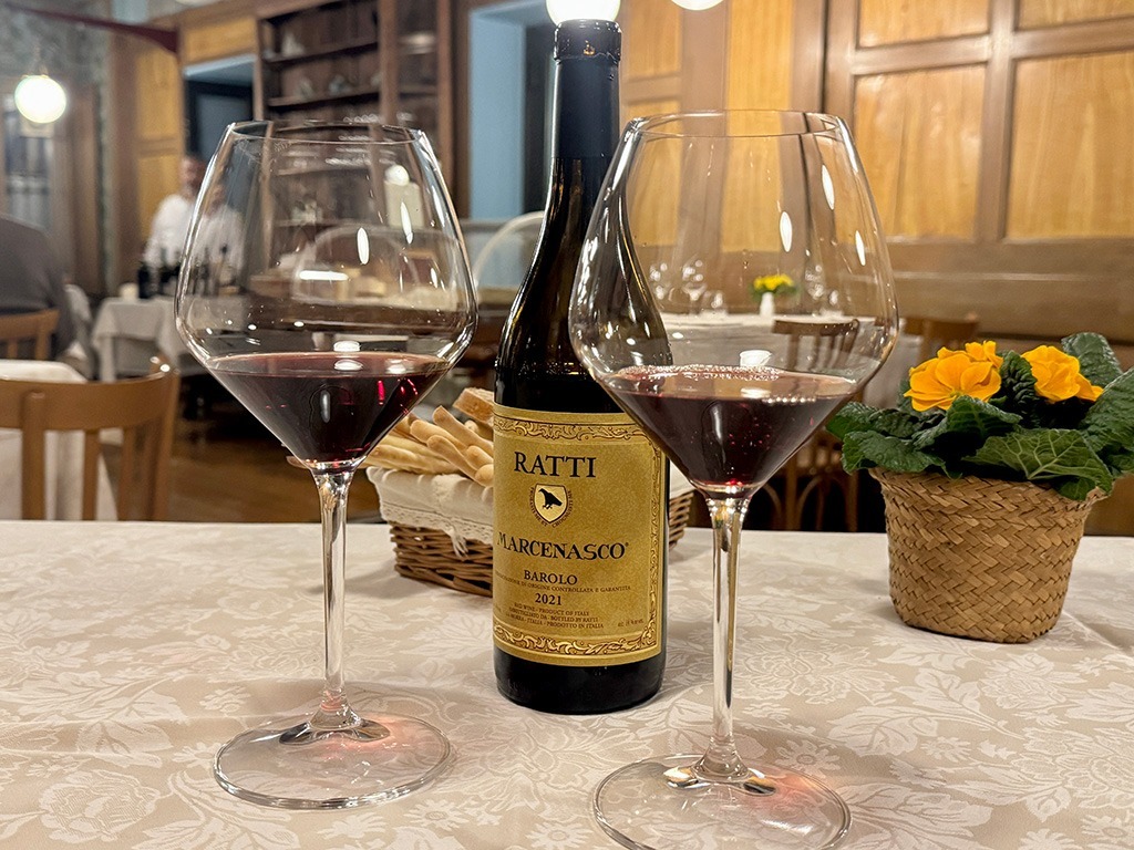 two glasses of red wine and bottle of Barolo on white tablecloth