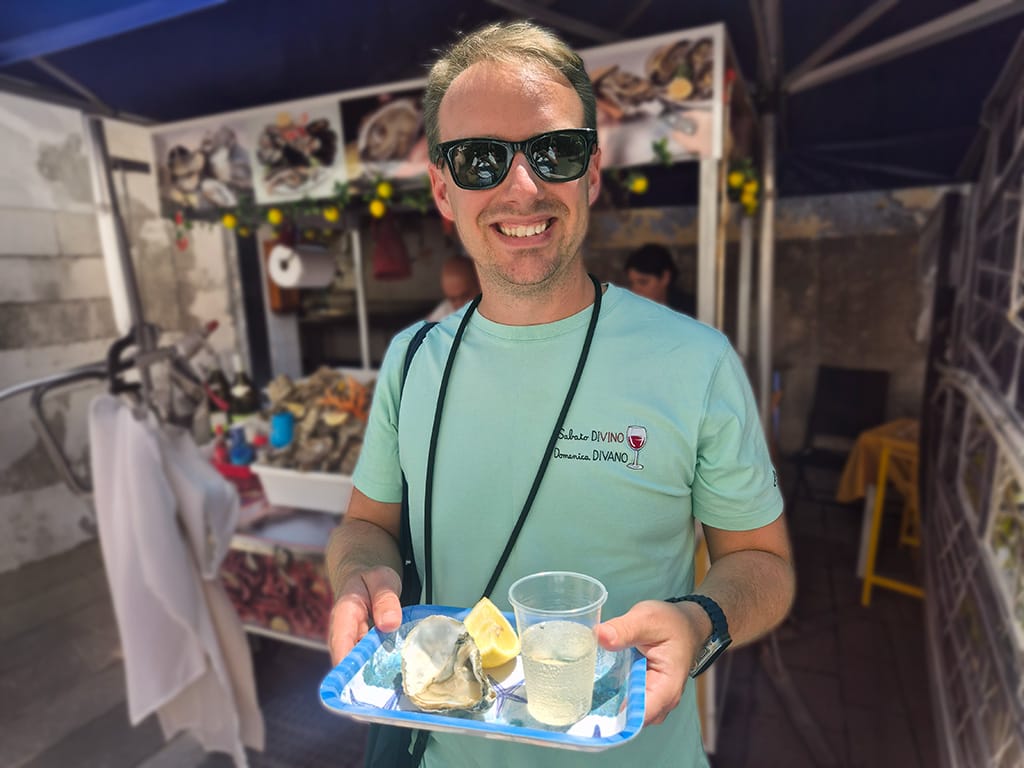 image of Warren smiling with a plate of oysters, lemon and white wine at ortigia market