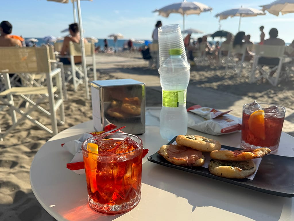 beach aperitivo with negroni glasses, bottle water and snacks on the sand