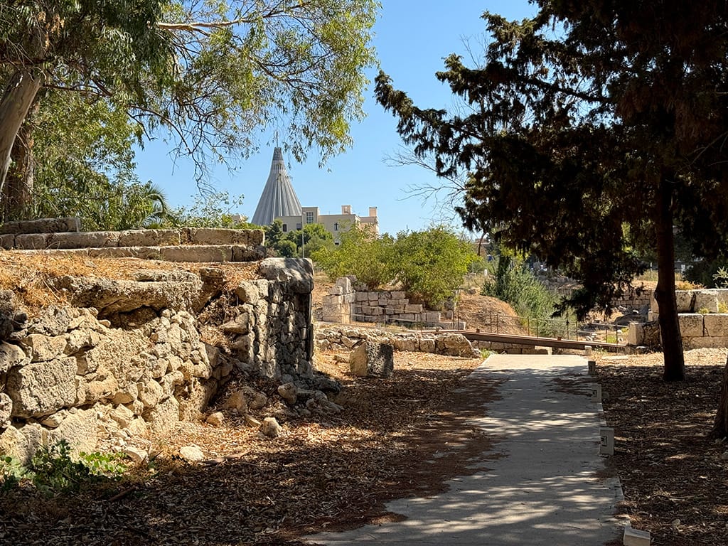 view across ruins in Neapolis Archaeological Park with spire of modern cathedral in distance